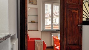 A room with a wooden door, a red sofa, a white radiator, and a window with a view of buildings. - JOIVY Welcoming flat in Porta Garibaldi (Milan)