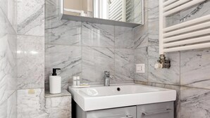 A bathroom with a white sink, marble walls, a mirror, and a towel rack. - JOIVY Welcoming flat in Porta Garibaldi (Milan)