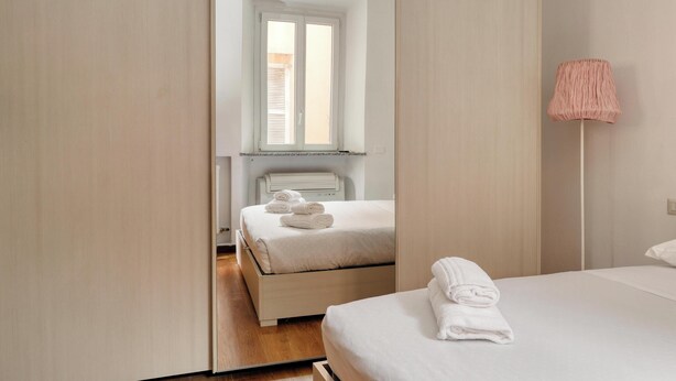 A modern hotel room with a large bed, a bedside table, a lamp, and a window with blinds. - JOIVY Welcoming flat in Porta Garibaldi (Milan)