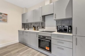 Uma cozinha moderna com armários cinzas, forno embutido e micro-ondas.