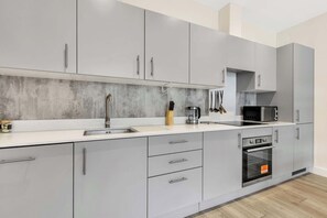 Uma cozinha moderna com armários cinza, forno de aço inoxidável e micro-ondas.