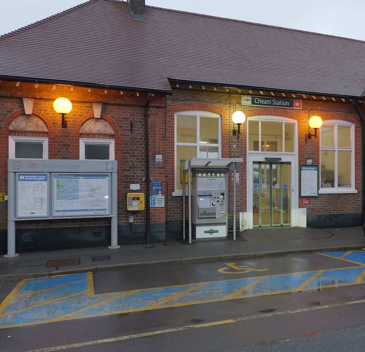 A brick building with a sign for Cheam Station, a ticket machine, and a map display.