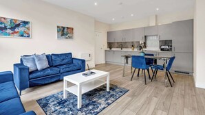 A modern living room with a blue sofa, a white coffee table, and a dining area with blue chairs.