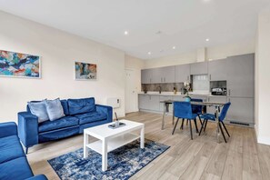 Uma sala de estar moderna com um sofá azul, uma mesa de centro branca e uma área de jantar com cadeiras azuis.