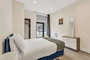 Quarto moderno com uma cama grande, mesa de cabeceira, cômoda e janela com vista para a rua.