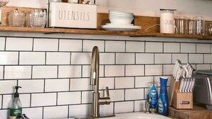 Een keuken met witte metrotegels, een roestvrijstalen spoelbak, houten werkbladen en planken met keukengerei, glazen en servies.
