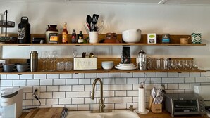 Een keuken met een witte betegelde achterwand, houten planken en diverse keukenbenodigdheden en apparaten.