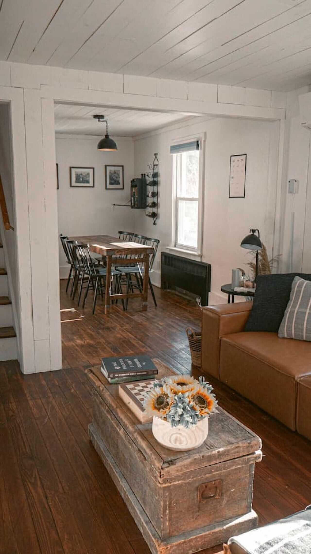 A spacious living room with a wooden dining table, a brown leather sofa, and a vintage trunk as a coffee table.