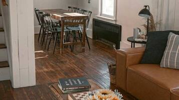 A spacious living room with a wooden dining table, a brown leather sofa, and a vintage trunk as a coffee table.