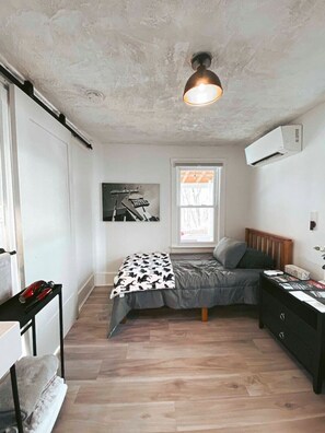 A bedroom with a bed, a desk, a window, and an air conditioner. - Charming Mtn Stay | Views, Hot Tub, Prime Location (West Kill)