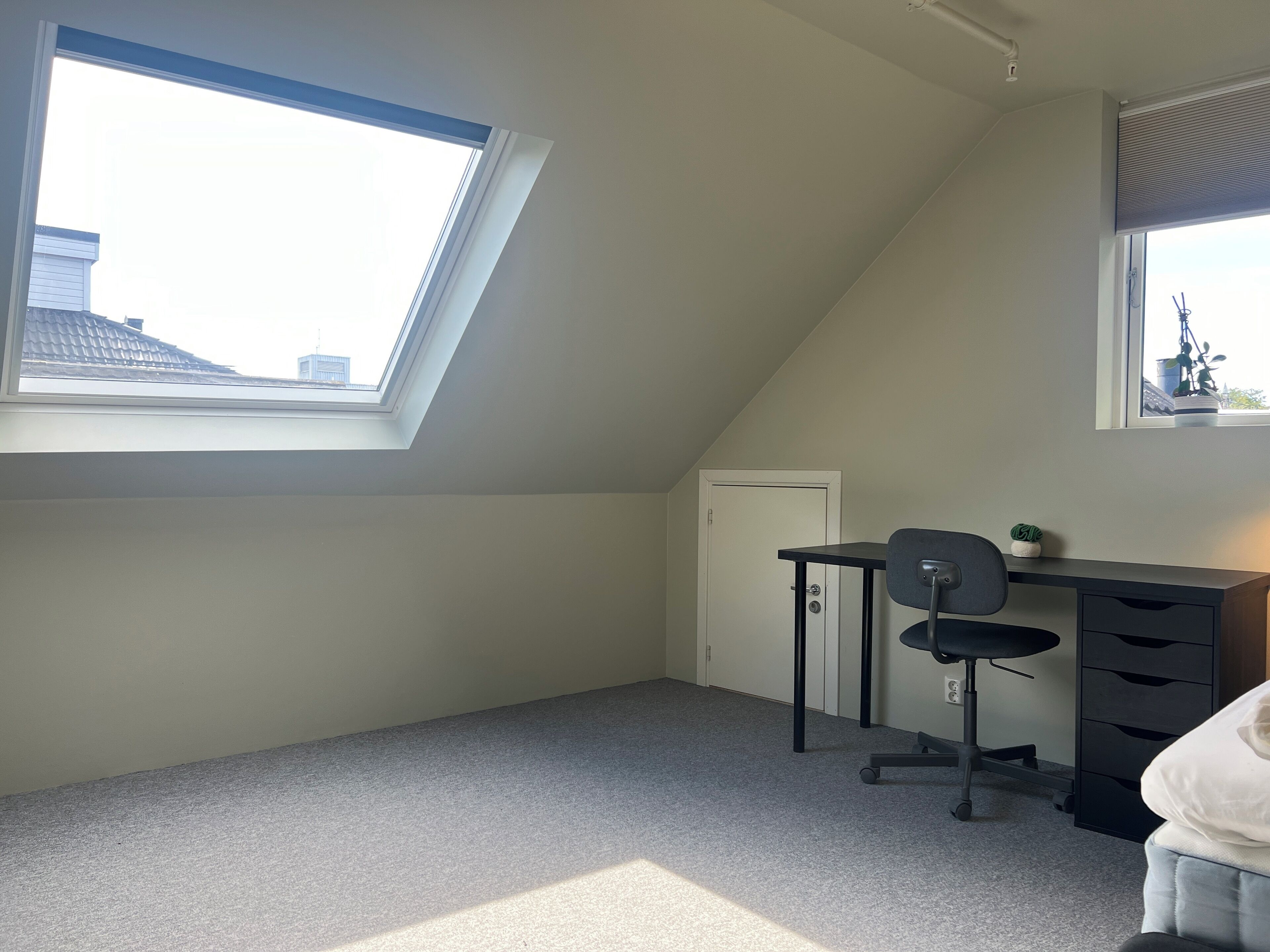 Ein kleines, helles Schlafzimmer im Dachgeschoss mit Oberlicht, Schreibtisch und Stuhl.