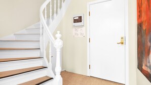 A staircase with white balusters and wooden steps, a white door with a gold handle, and a thermostat on the wall. - Central Guest House (Stavanger)