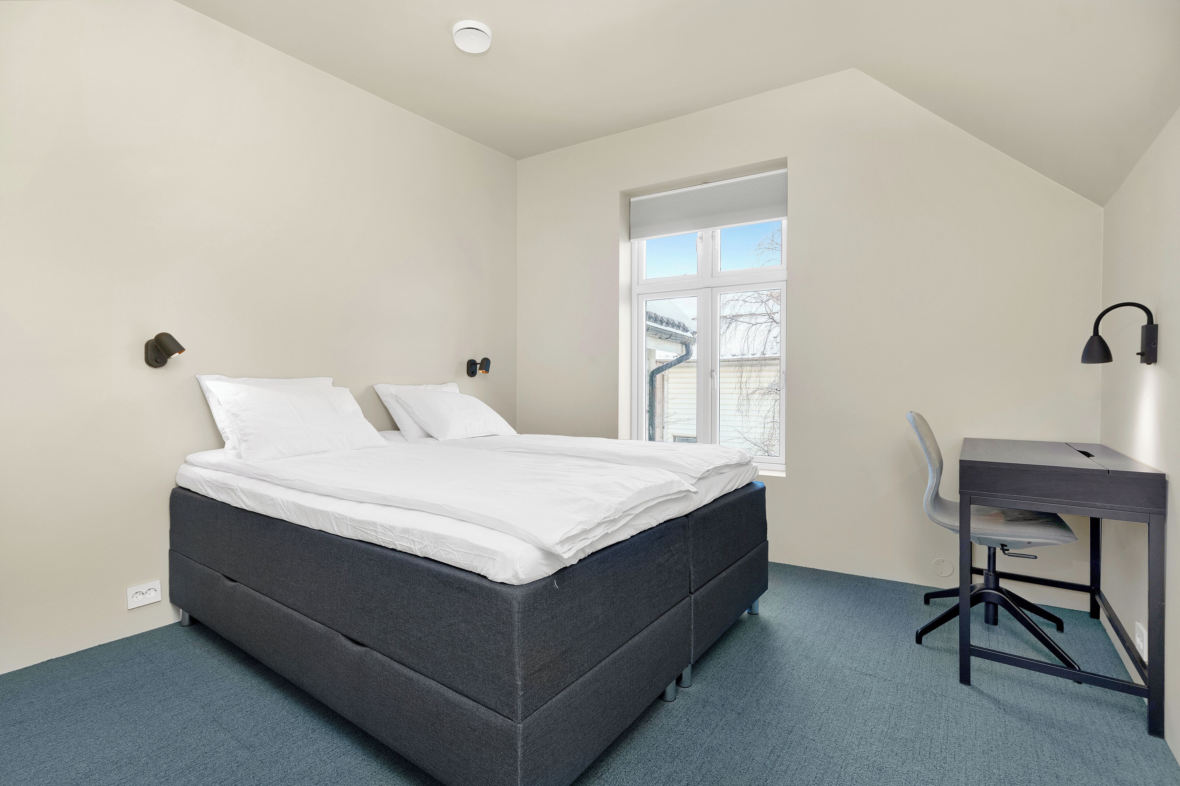 A bedroom with a bed, a desk, and a chair.