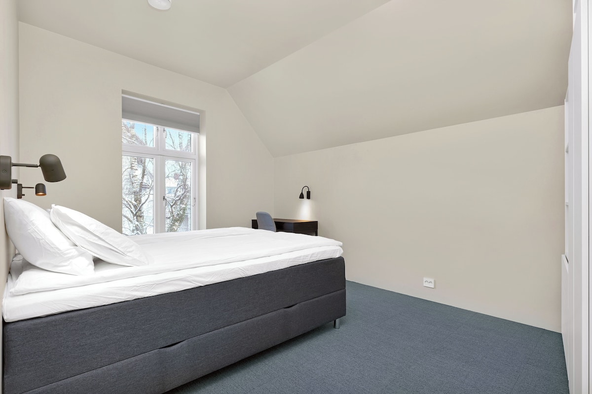 Un dormitorio con cama, mesita de noche, lámpara y ventana.