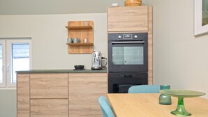 A compact kitchen with wooden cabinets, a built-in oven, and a dining table with a green glass table runner. - Central Guest House (Stavanger)