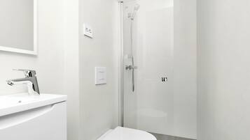 A modern bathroom with a white sink, toilet, and glass-enclosed shower.