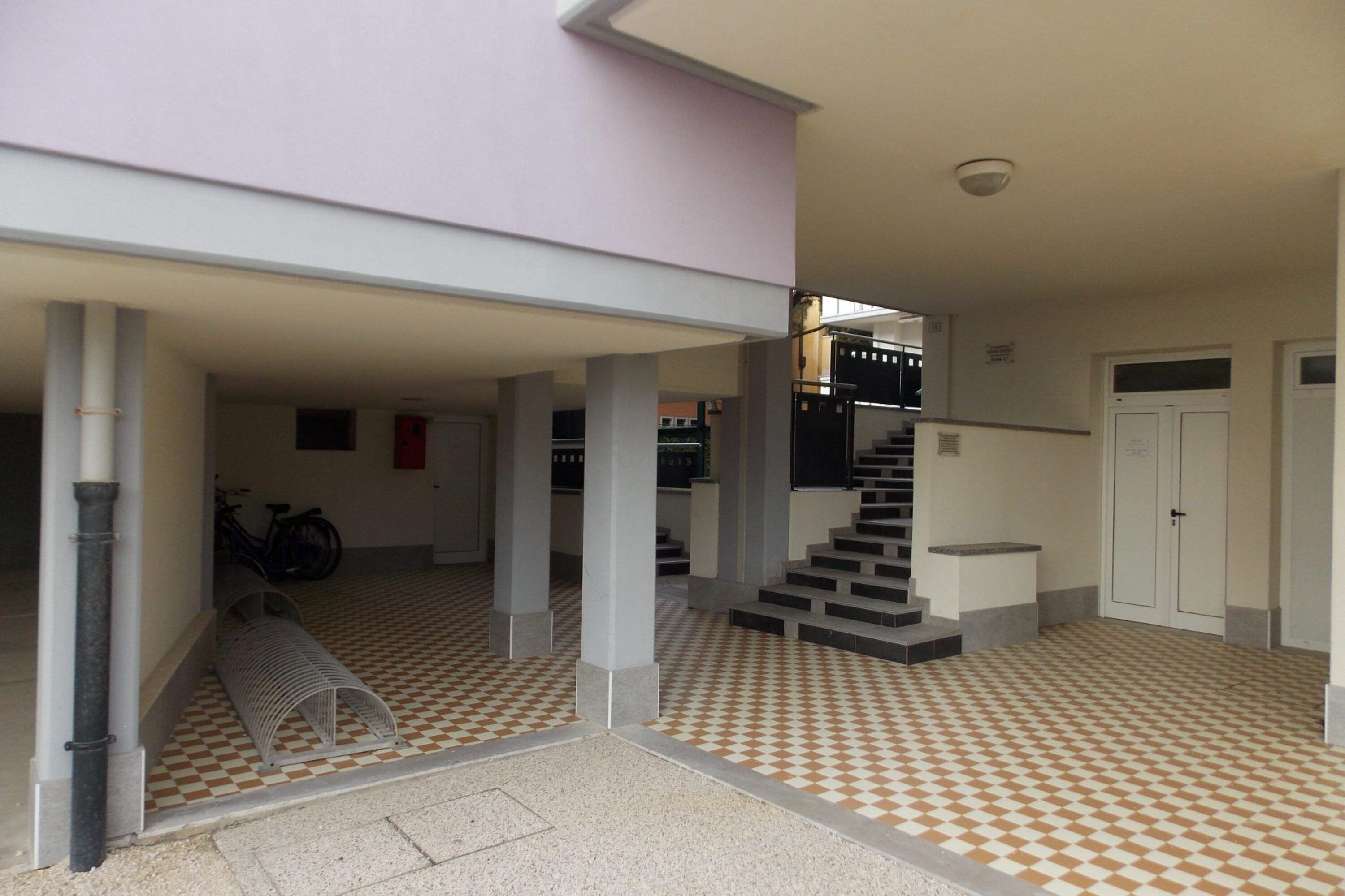 A spacious indoor area with a checkered floor, a staircase, and a bicycle in the background.
