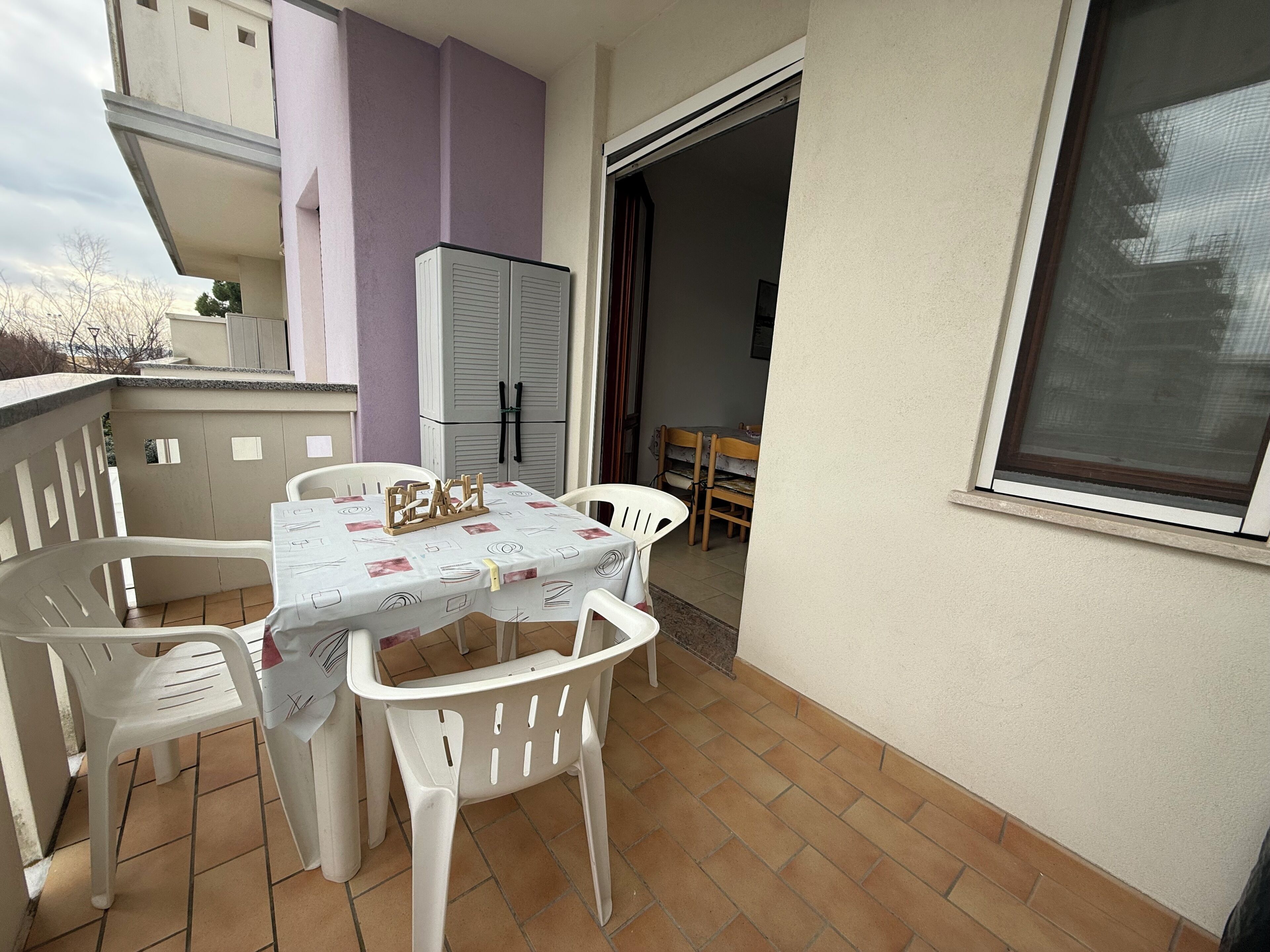 Un piccolo balcone esterno con tavolo e sedie, un frigorifero e una finestra.