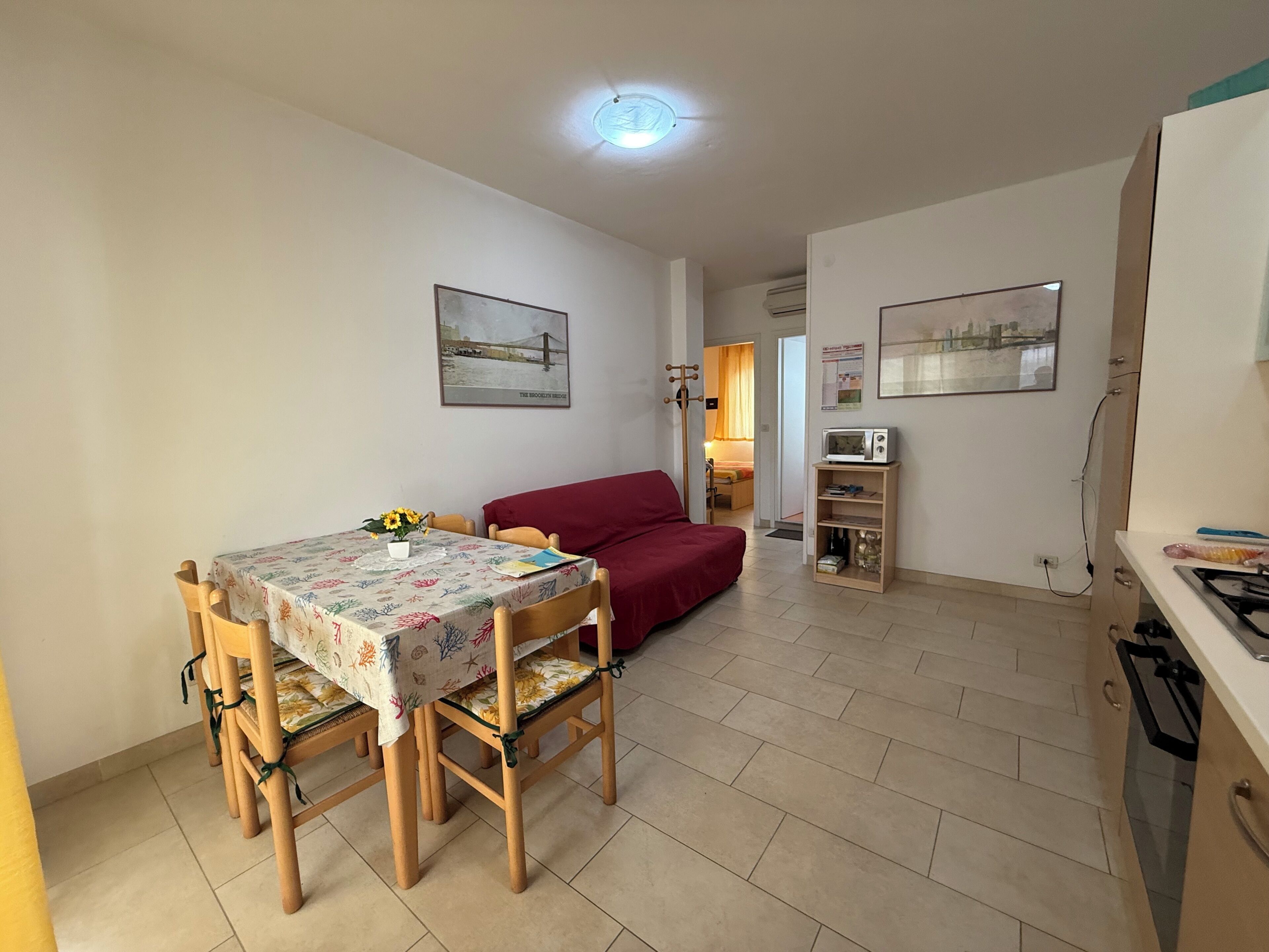 Un coin repas avec une table et des chaises, un canapé rouge et une cuisine équipée d’un four à micro-ondes et d’une cuisinière.