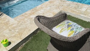 Una piscina con dos flotadores, una silla de mimbre con cojín y dos sillas verdes.