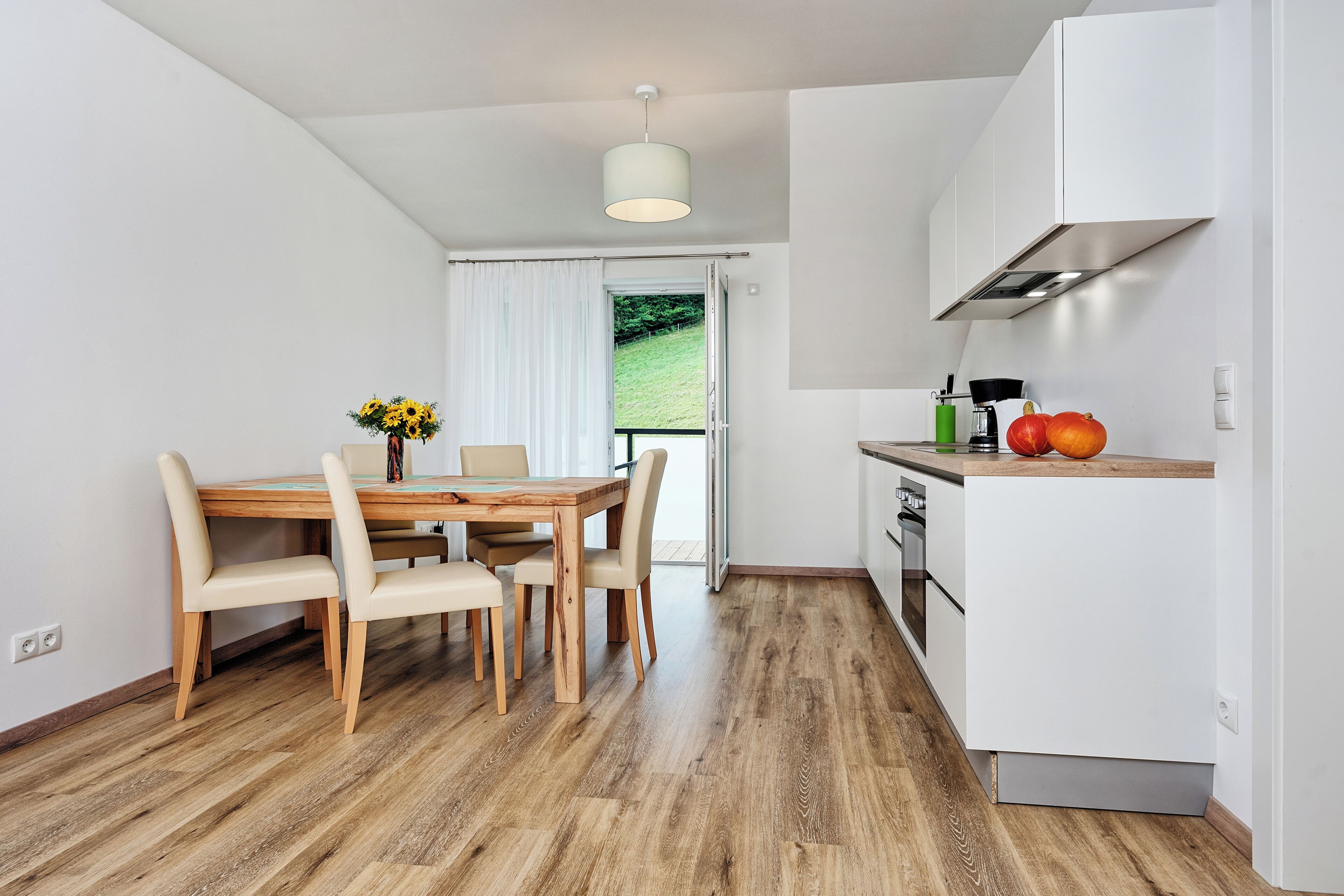 Una cocina moderna con armarios blancos, una mesa de comedor de madera con sillas y vistas al exterior.