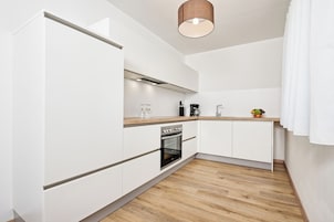 Una cocina moderna con armarios blancos, encimera de madera, horno integrado y una lámpara colgante.
