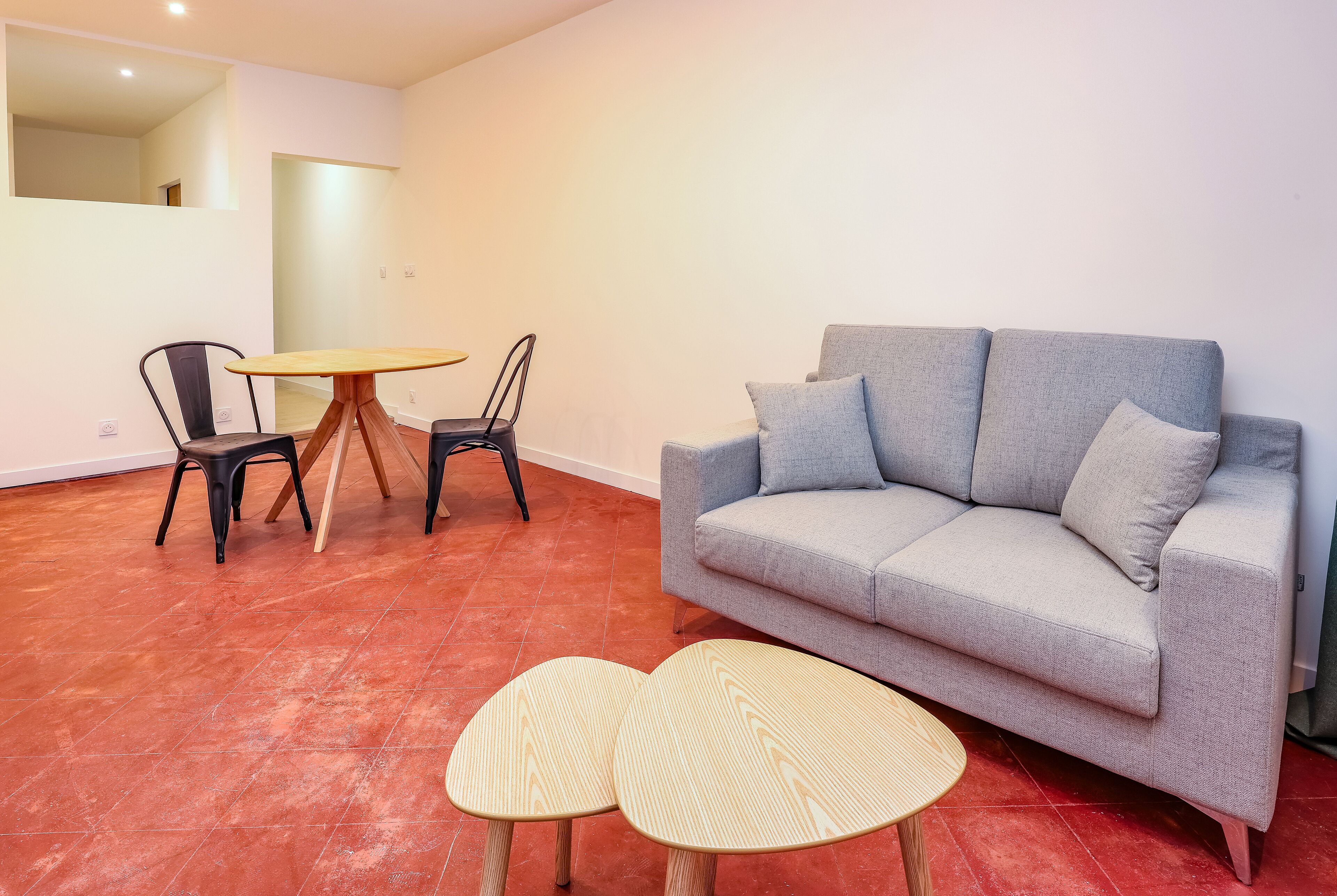 A living room with a grey sofa, two chairs, a round table, and two small wooden tables.