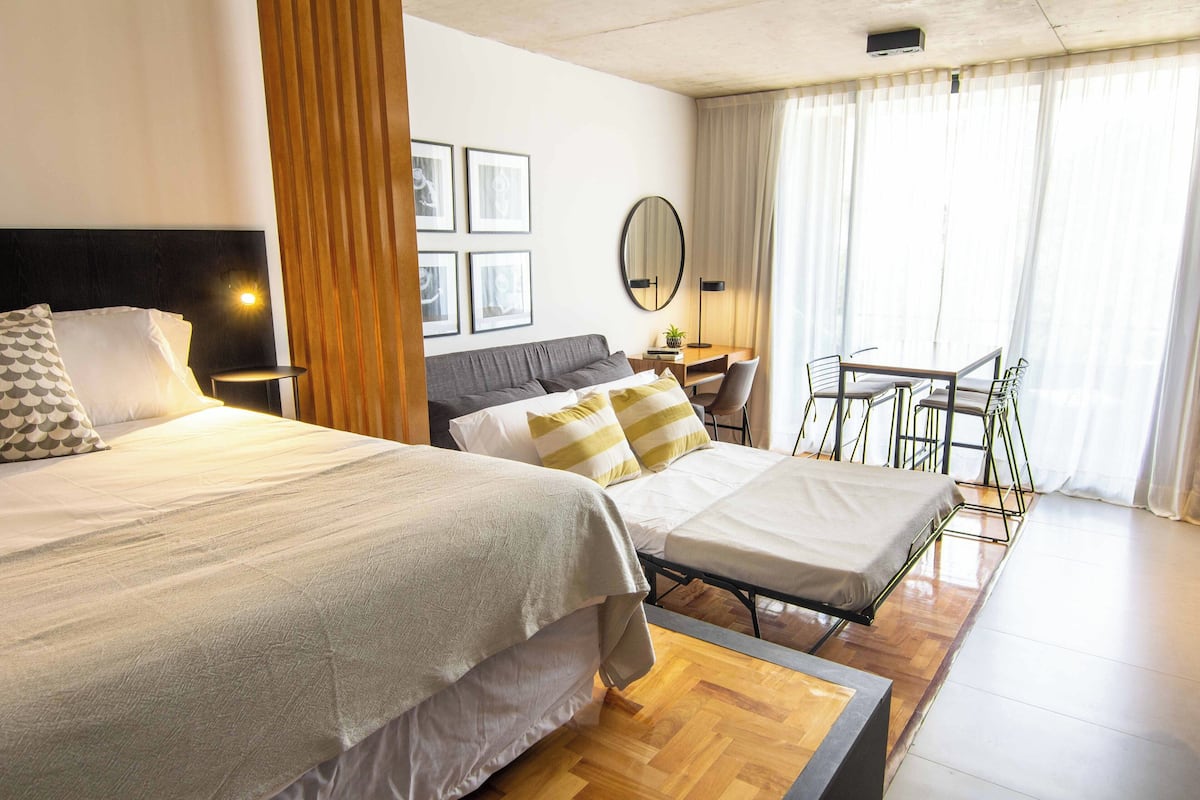 Habitación de hotel con dos camas, un escritorio, una silla, un espejo y vistas al exterior.