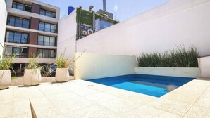 Un espace piscine extérieur moderne, avec une piscine bleue, des plantes en pot et un bâtiment en arrière-plan.