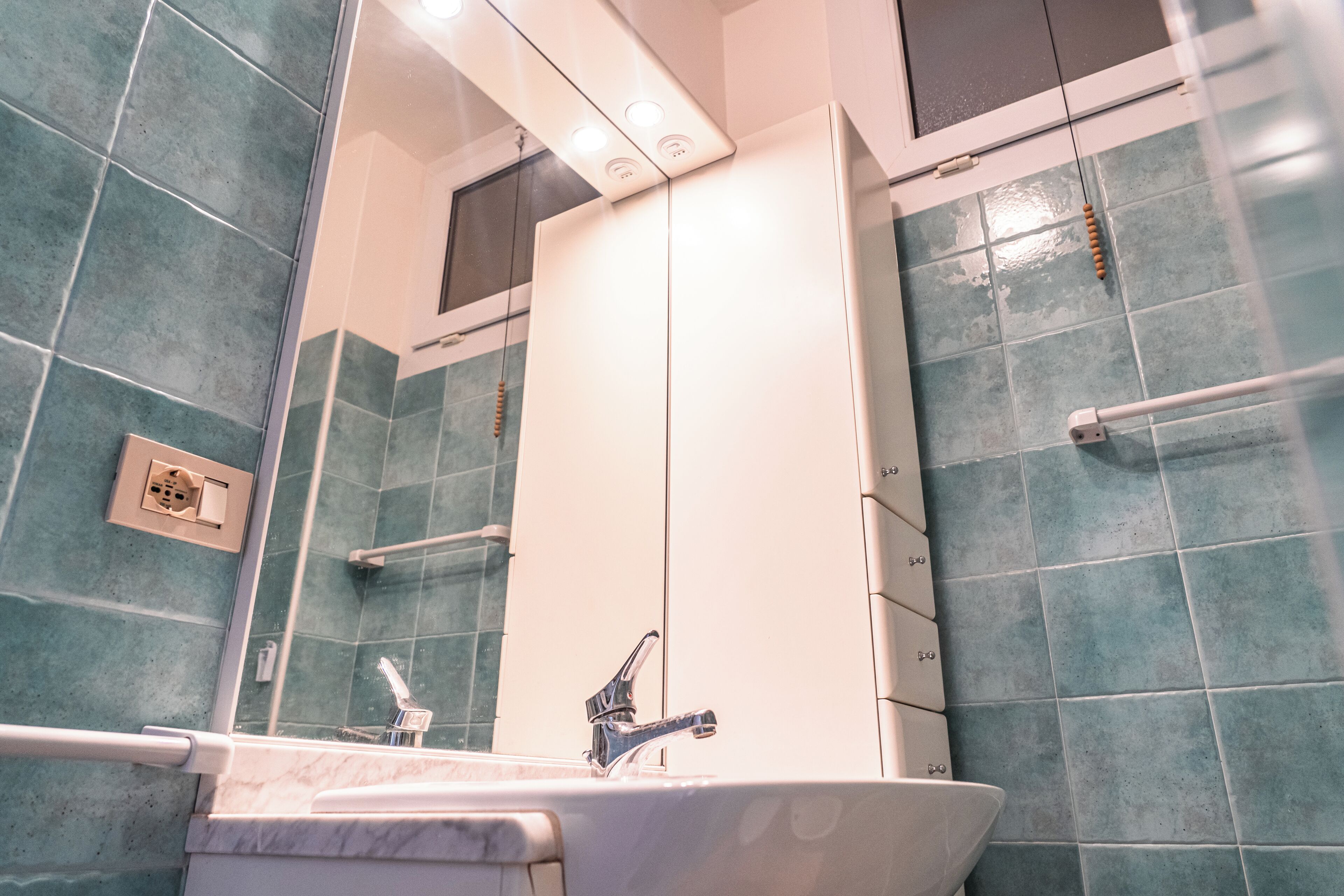 A bathroom with a white sink, a mirror, and blue-tiled walls.