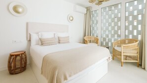 Ein Schlafzimmer mit einem großen Bett, zwei Korbstühlen, einem kleinen runden Tisch und einer dekorativen Wandverkleidung.