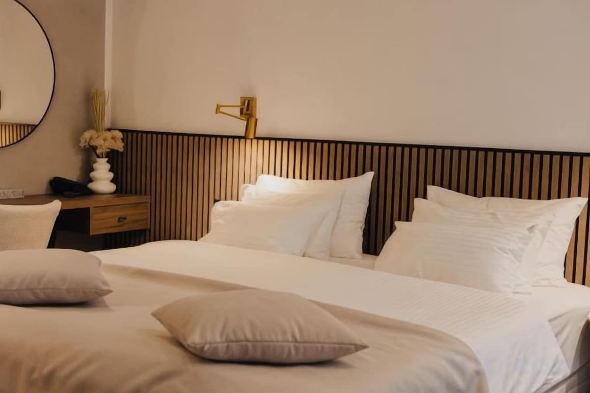 A hotel room with a large bed, a bedside table, a mirror, and a wall-mounted lamp.