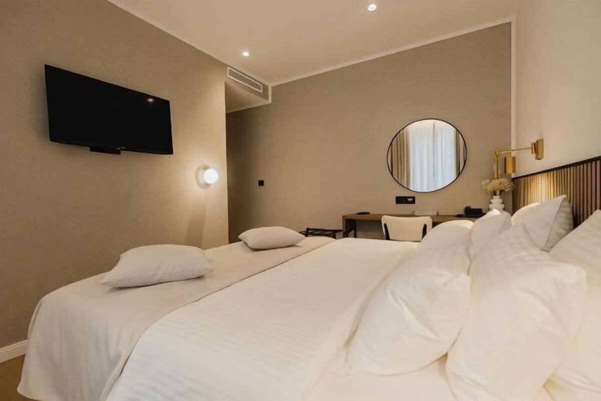 A hotel room with two beds, a television, a round mirror, and a bedside table with a lamp.