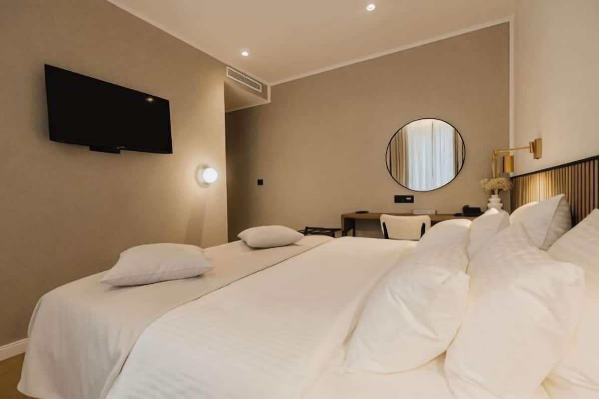 Habitación de hotel con dos camas, un televisor, un espejo redondo y una mesita de noche con lámpara.