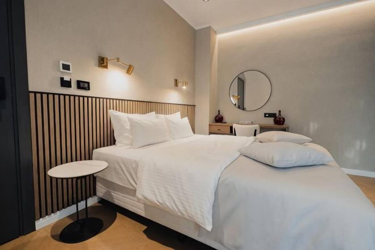 A modern hotel room with a bed, bedside tables, a round mirror, and a small round table.