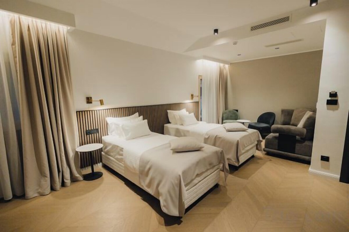 A hotel room with two beds, a sofa, a small table, and a curtain.