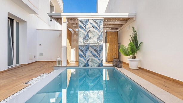 Ein moderner Poolbereich mit klarem, blauem Pool, Holzbelag und Wand mit tropischem Blattmuster.