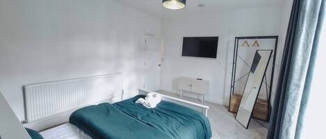 Une chambre à coucher moderne avec un lit, une commode blanche, un miroir et un téléviseur fixé au mur.