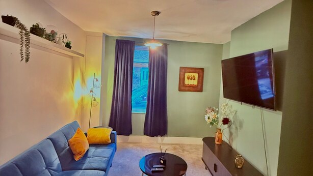 A living room with a blue sofa, a coffee table, a flat-screen TV, and a wall-mounted TV. - Bristol City Center - Cosy 2 Bedroom House (Bristol)