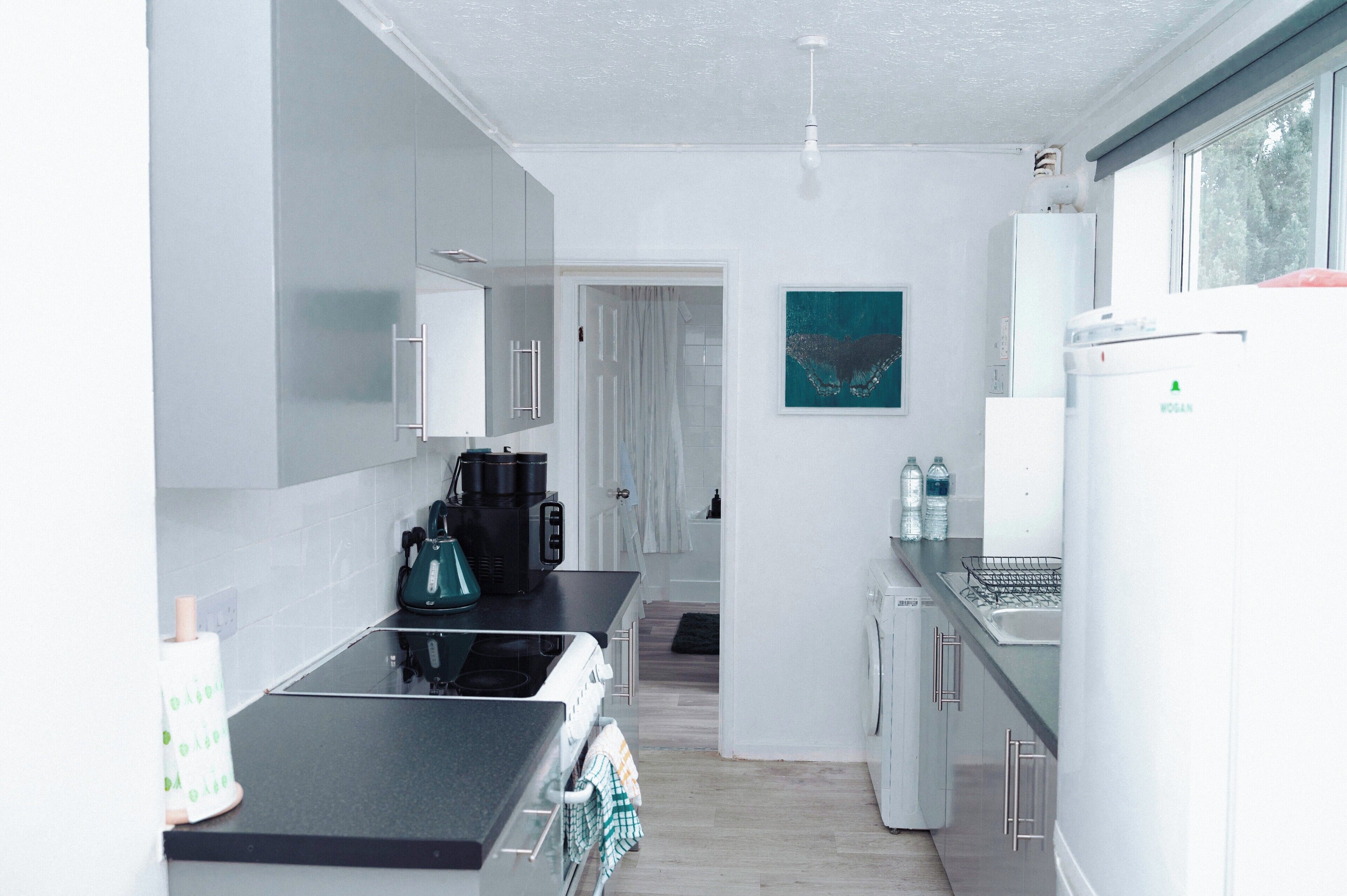 Cocina moderna con encimera negra, armarios blancos y vistas al baño contiguo.