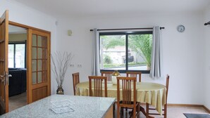 Comedor con mesa dispuesta para cuatro personas, sillas de madera, encimera de granito y ventana con cortinas.