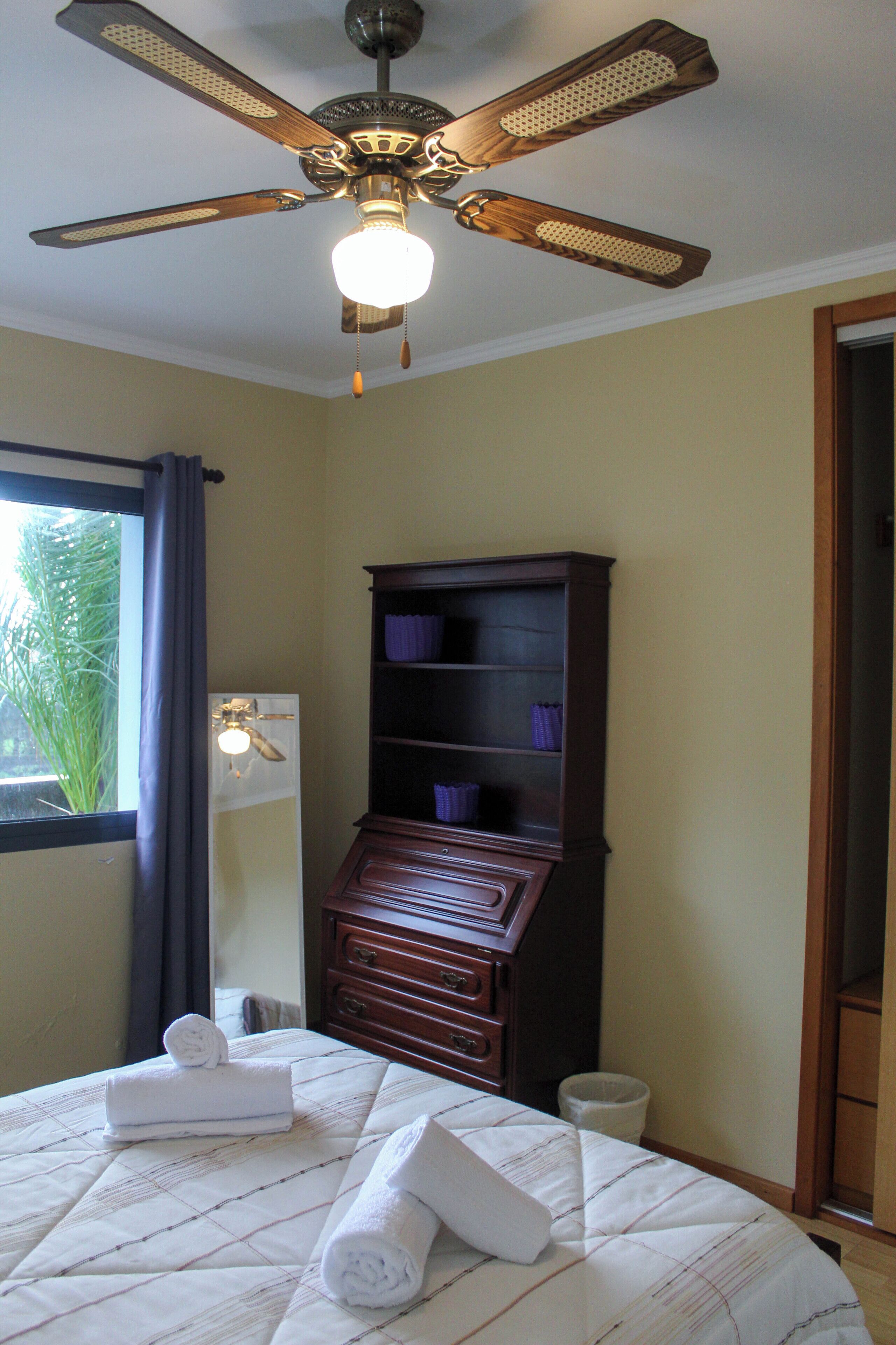 A hotel room with a bed, a ceiling fan, a nightstand, a dresser, and a window with curtains.