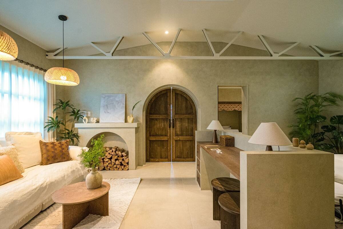 A living room with a sofa, coffee table, and a fireplace. There is a wooden door and a mirror on the wall.