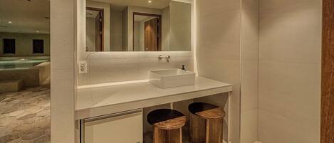 A modern bathroom with a large mirror, a white sink, and two wooden stools.