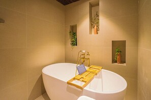 Un baño moderno con una bañera independiente, una bandeja de madera y dos macetas en la pared.