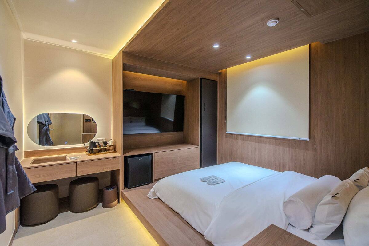 A modern hotel room with a wooden vanity, a bed, a television, and a large mirror.