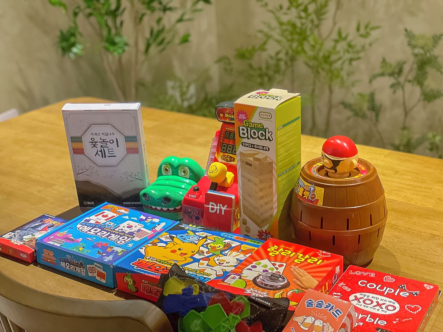 Une variété de jouets et de jeux colorés sont disposés sur une table, notamment un dinosaure jouet vert, un robot jouet rouge et un tonneau en bois sur lequel repose une balle rouge.