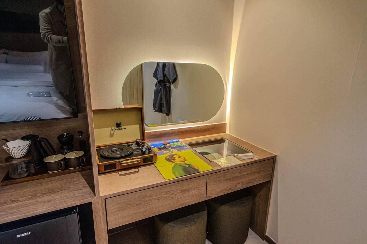 A hotel room with a wooden desk, a mirror, a bed, and a television.