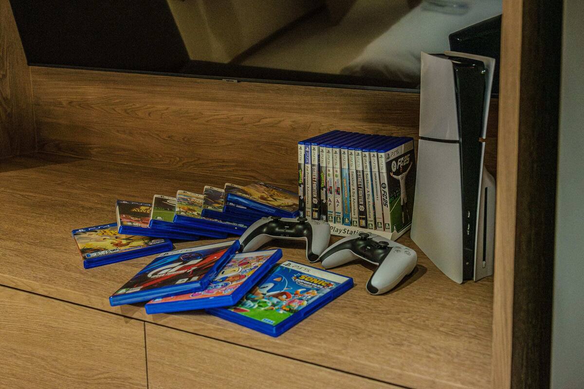 A wooden floor with a PlayStation 5 console, controllers, and a collection of video games.