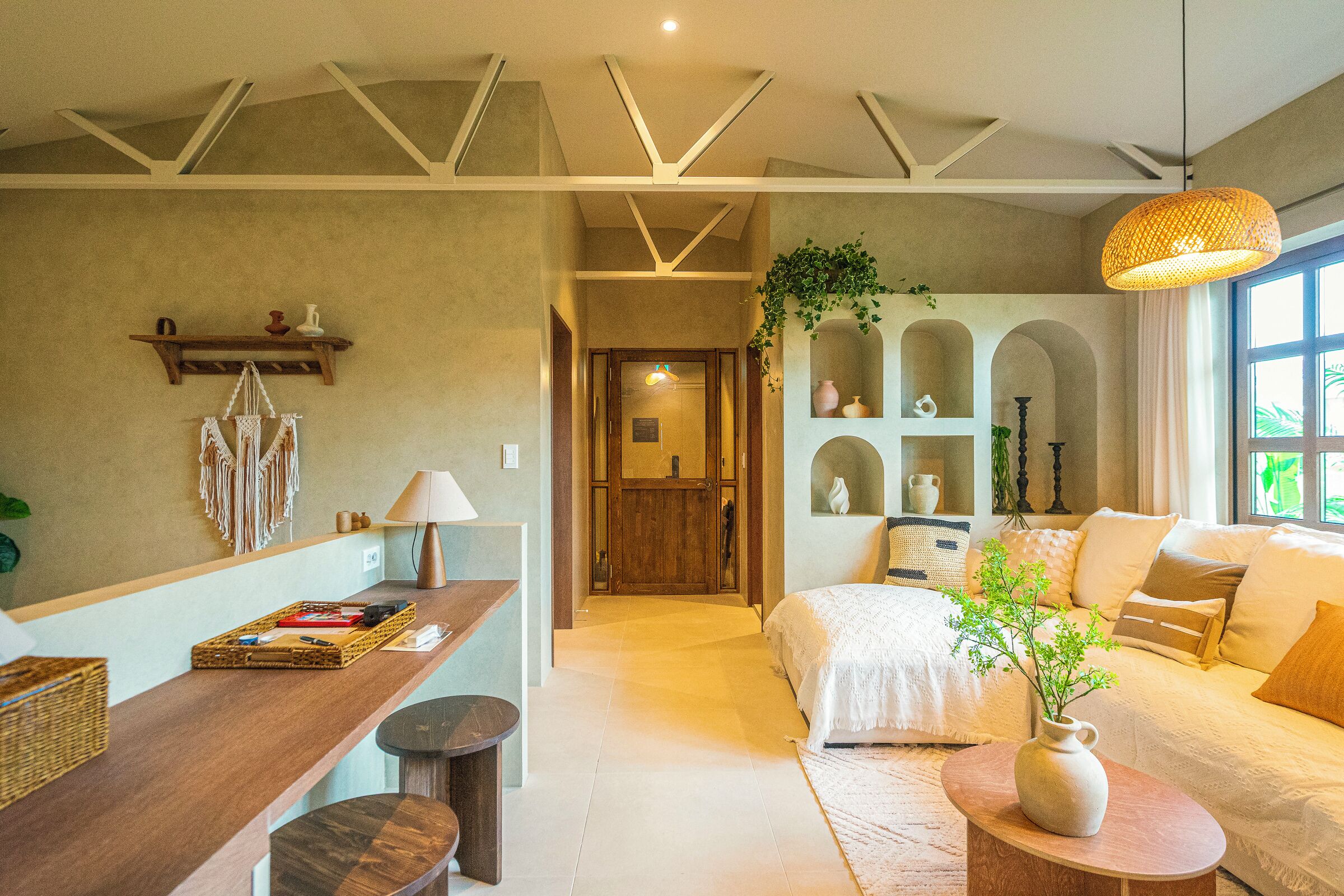 Una camera d'albergo moderna con una scrivania in legno, un letto con copriletto bianco, un tavolo rotondo in legno con un vaso e un'ampia finestra vista verde.